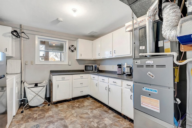 kitchen featuring stainless steel microwave, heating unit, dark countertops, and white cabinets