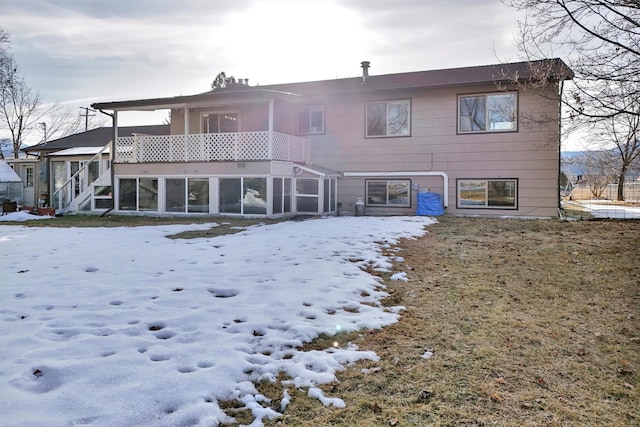 snow covered rear of property with a balcony and a sunroom