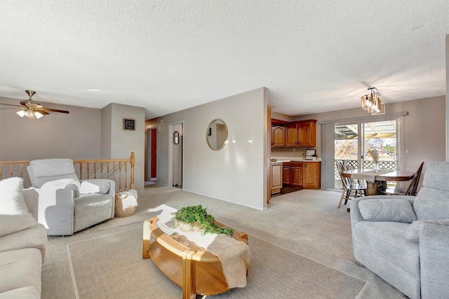 living room featuring ceiling fan with notable chandelier, light colored carpet, a textured ceiling, and baseboards