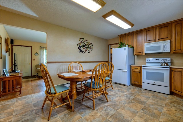 kitchen with brown cabinets, stone finish flooring, a textured ceiling, white appliances, and light countertops