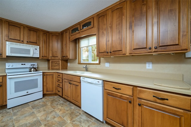 kitchen with light countertops, brown cabinets, white appliances, a textured ceiling, and a sink