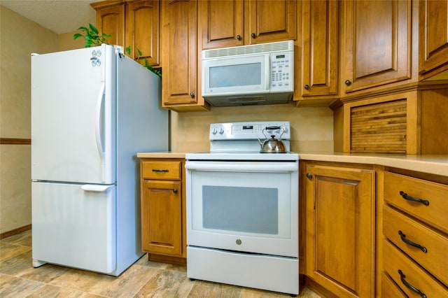 kitchen featuring white appliances, brown cabinetry, and light countertops