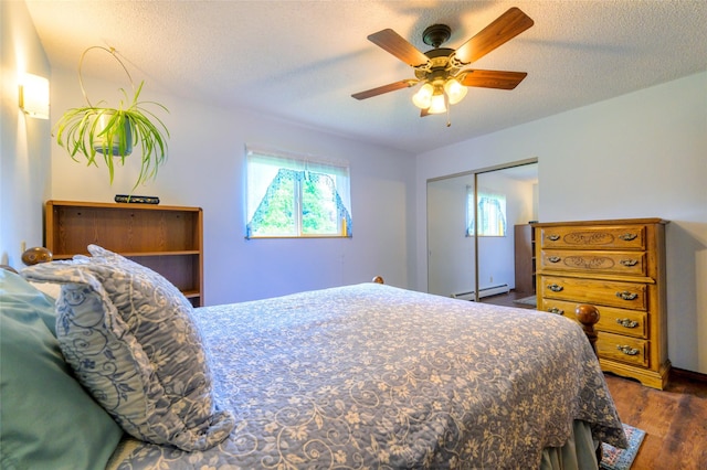 bedroom with a closet, a textured ceiling, a baseboard heating unit, and dark wood-type flooring