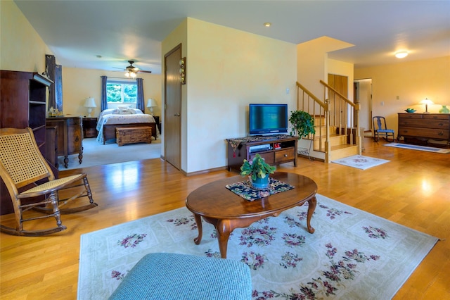 living area with a ceiling fan, stairs, baseboards, and wood finished floors