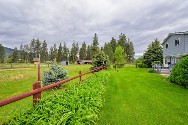 view of yard featuring a rural view, an outdoor structure, and fence