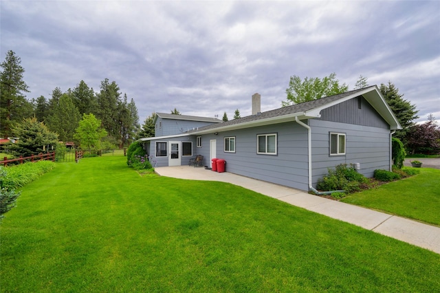 rear view of house with a yard, fence, a chimney, and a patio area