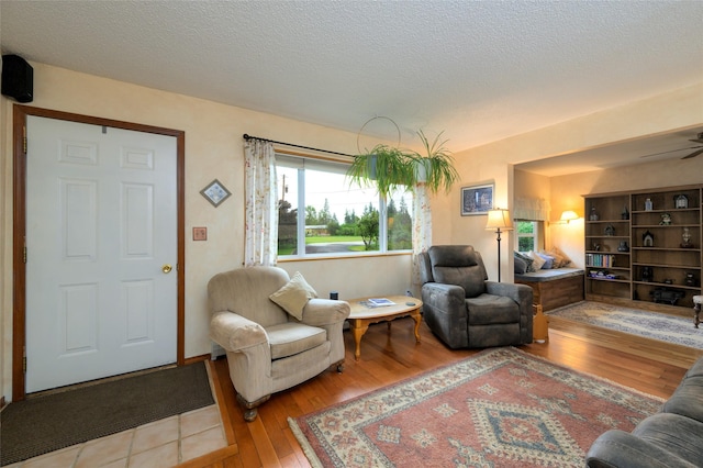 living room with a textured ceiling, ceiling fan, and hardwood / wood-style flooring