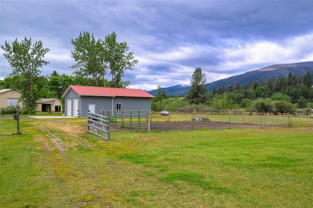 view of yard with fence, a pole building, an outdoor structure, a detached garage, and a mountain view