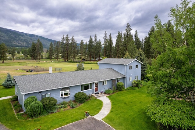 view of front of home with a front yard, a mountain view, and a shingled roof