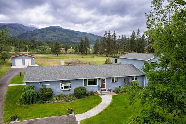 view of front facade with an outbuilding, a shingled roof, a front lawn, a detached garage, and a mountain view