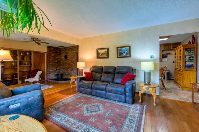 living area with a brick fireplace, a textured ceiling, ceiling fan, and hardwood / wood-style flooring