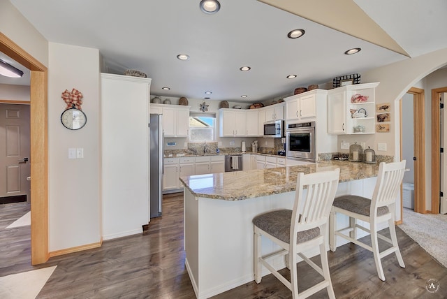 kitchen with dark wood-style floors, stainless steel appliances, arched walkways, a peninsula, and light stone countertops