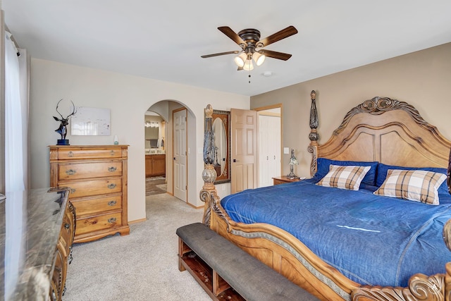 bedroom with connected bathroom, arched walkways, light carpet, and a ceiling fan