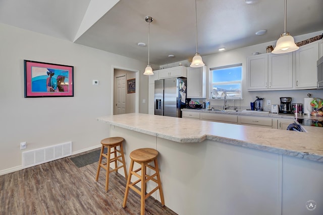 kitchen with visible vents, a sink, a breakfast bar, stainless steel fridge, and dark wood-style flooring