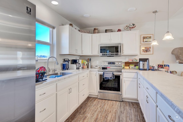 kitchen featuring light wood-type flooring, a sink, white cabinetry, stainless steel appliances, and light countertops