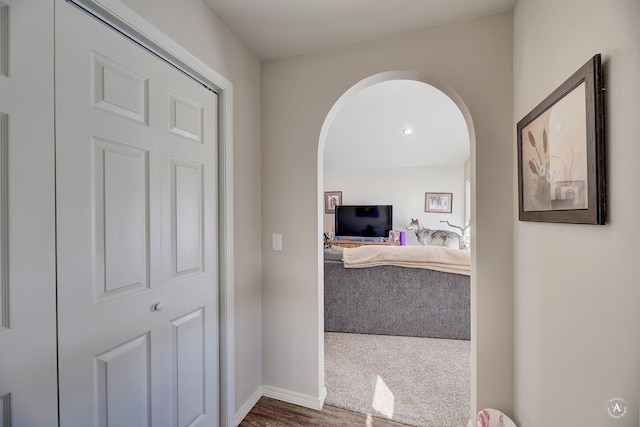 corridor featuring baseboards, arched walkways, and wood finished floors