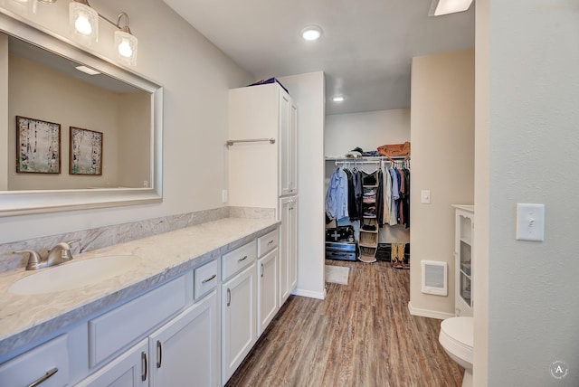 full bathroom featuring visible vents, a walk in closet, toilet, wood finished floors, and vanity