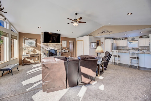 living room featuring vaulted ceiling, light carpet, a stone fireplace, recessed lighting, and a ceiling fan