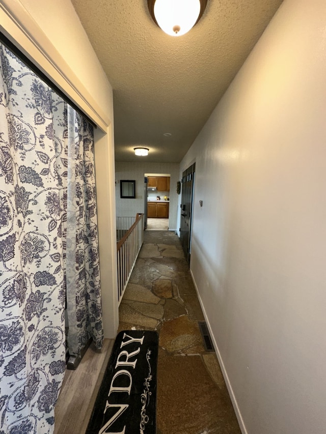 hall featuring visible vents, stone finish floor, a textured ceiling, and baseboards