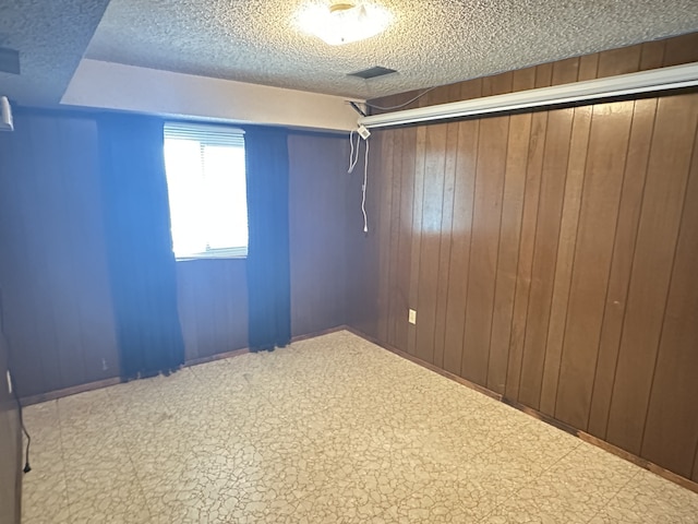 empty room with tile patterned floors, wooden walls, and a textured ceiling