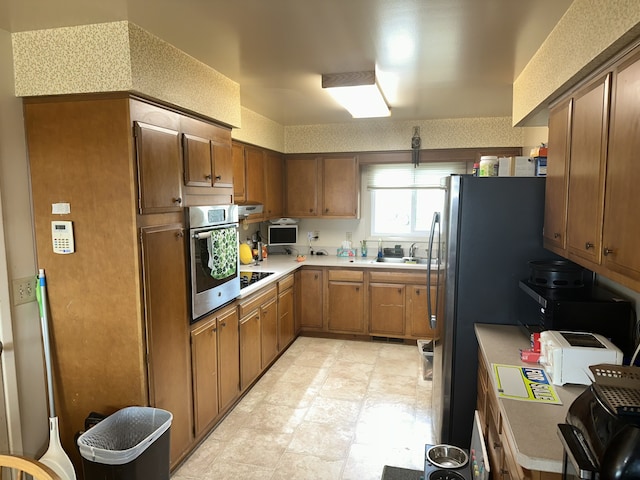 kitchen featuring light floors, a sink, light countertops, appliances with stainless steel finishes, and brown cabinets