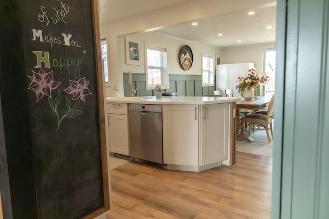 kitchen featuring light wood finished floors, a peninsula, a sink, light countertops, and dishwasher