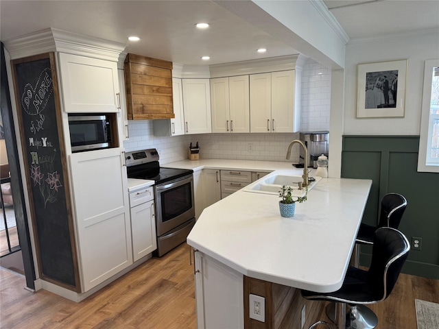 kitchen featuring a breakfast bar, ornamental molding, appliances with stainless steel finishes, a peninsula, and a sink