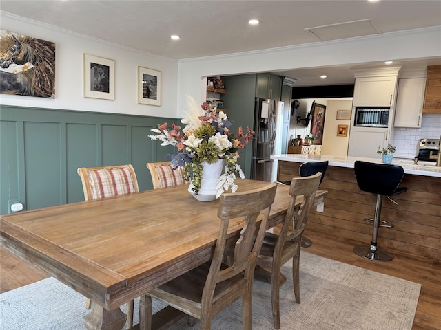 dining space featuring a wainscoted wall, attic access, recessed lighting, ornamental molding, and a decorative wall