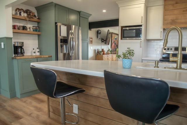 kitchen with backsplash, appliances with stainless steel finishes, a kitchen bar, and green cabinetry