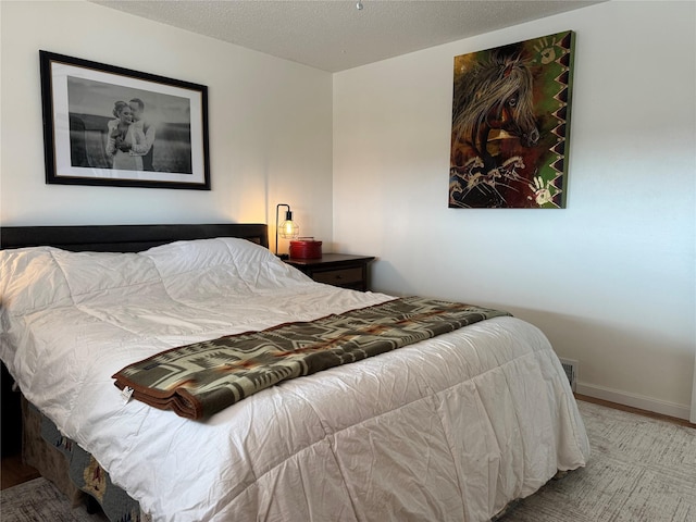 bedroom with wood finished floors, baseboards, and a textured ceiling