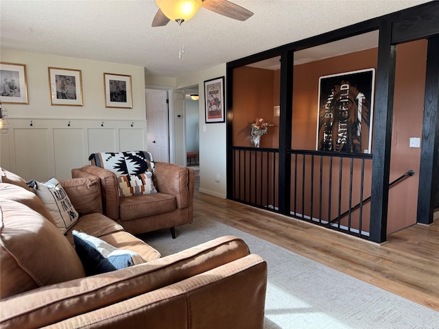 living area featuring ceiling fan, a textured ceiling, wood finished floors, and a decorative wall