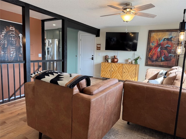 living room with ceiling fan, light wood-style floors, and a textured ceiling