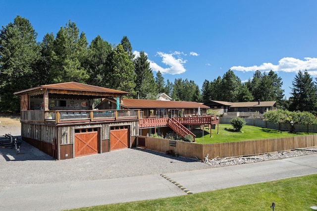 view of front of house with gravel driveway, a front lawn, an attached garage, and fence