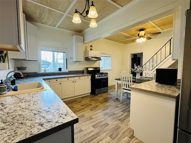 kitchen featuring stainless steel gas stove, a sink, white cabinetry, ceiling fan with notable chandelier, and light wood-type flooring