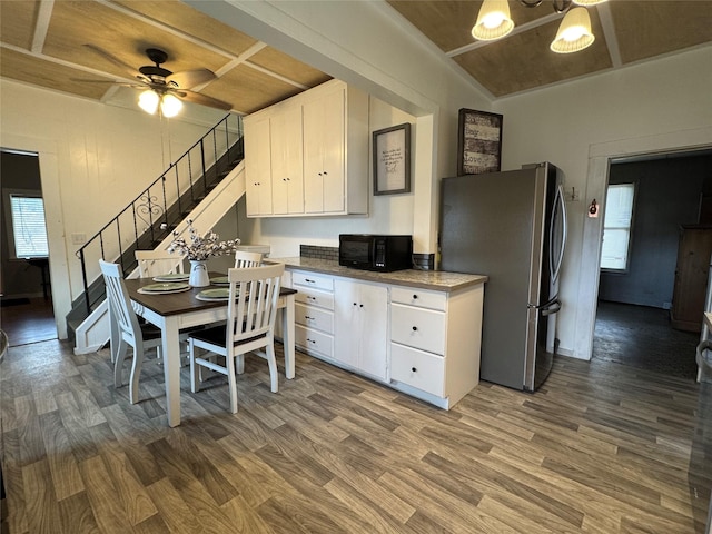 kitchen with white cabinets, wood finished floors, black microwave, and freestanding refrigerator