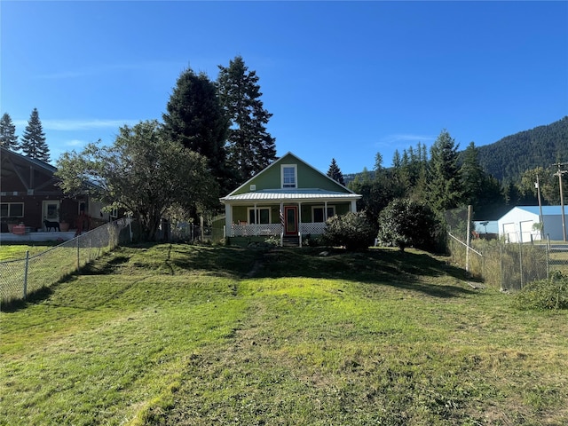 view of front of house featuring metal roof, covered porch, a front lawn, and fence