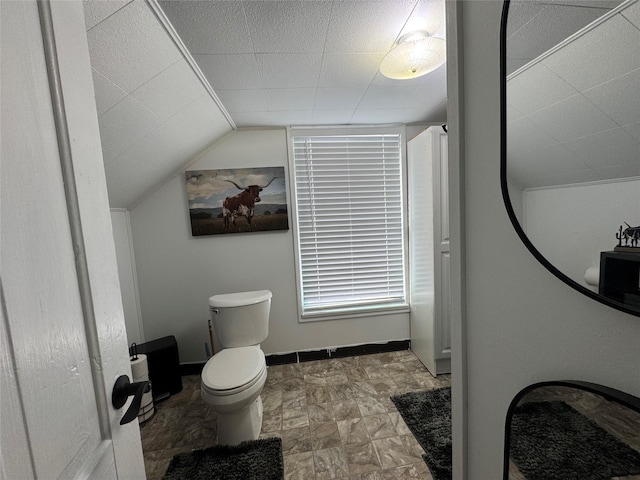 bathroom with vaulted ceiling, stone finish floor, toilet, and baseboards