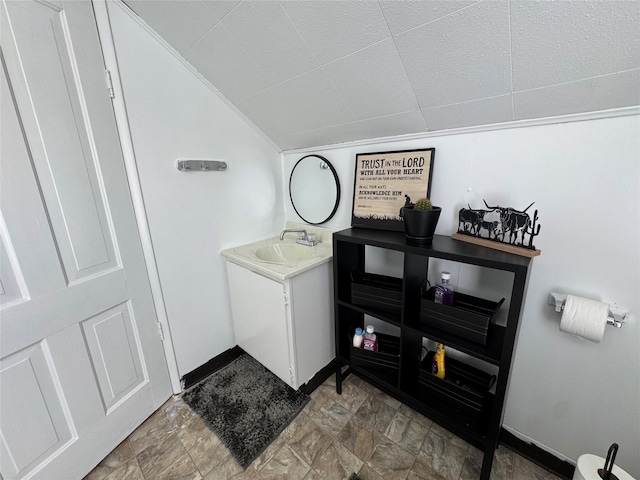 interior space with vanity, lofted ceiling, stone finish floor, and baseboards