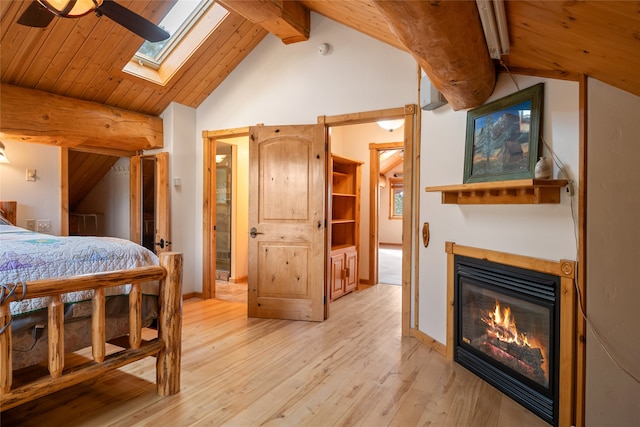 bedroom featuring a glass covered fireplace, vaulted ceiling with skylight, light wood-style floors, wooden ceiling, and baseboards