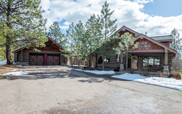 view of front of property featuring a porch, log siding, driveway, and an outdoor structure