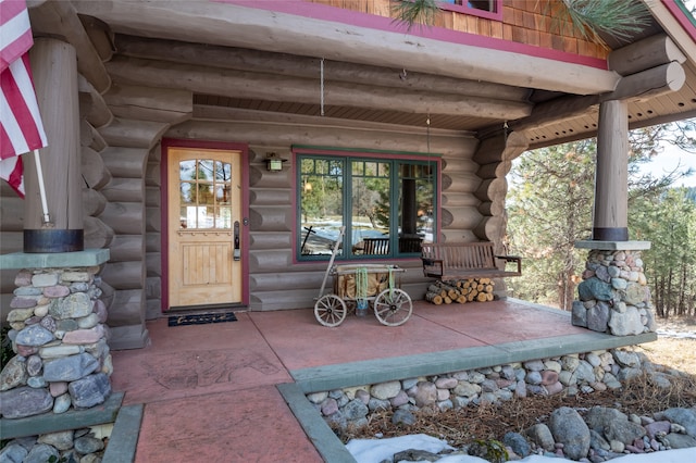 doorway to property featuring a porch and log siding