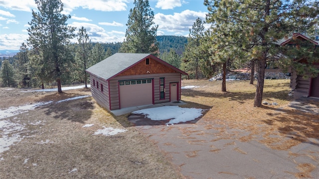 detached garage with driveway and a forest view