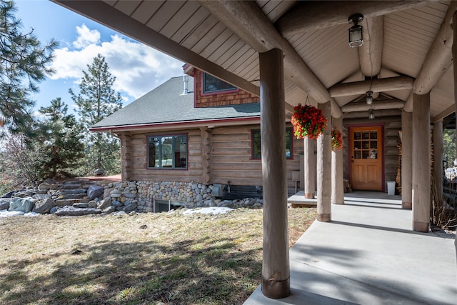 view of exterior entry featuring roof with shingles and log exterior