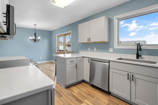 kitchen featuring light wood-style flooring, a sink, stainless steel appliances, a peninsula, and light countertops