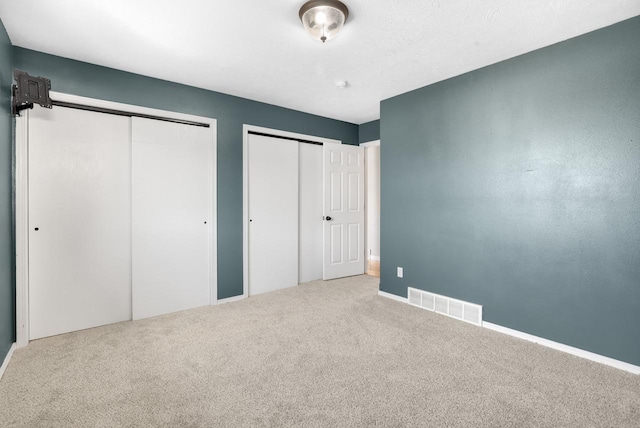 unfurnished bedroom featuring visible vents, carpet, and multiple closets