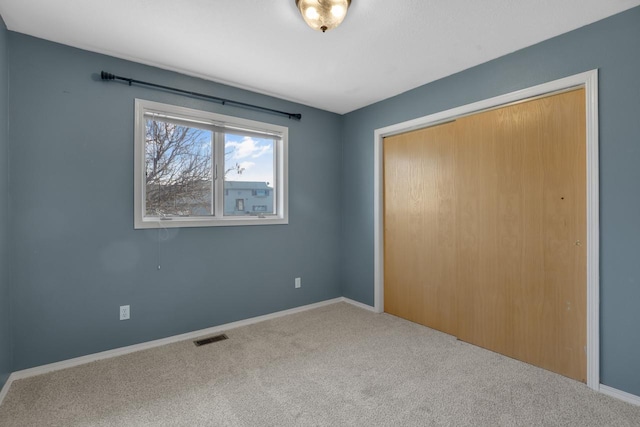 unfurnished bedroom featuring carpet, visible vents, a closet, and baseboards