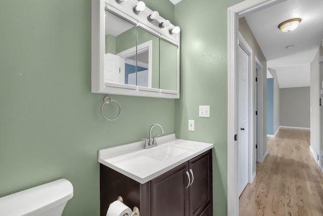 half bathroom featuring vanity, toilet, wood finished floors, and baseboards