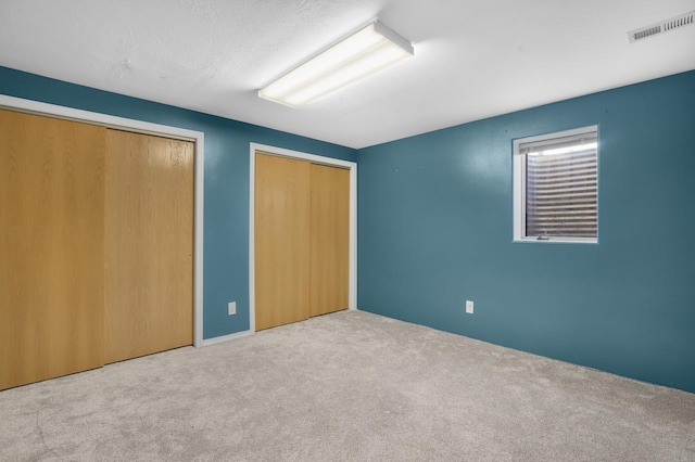 unfurnished bedroom featuring visible vents, two closets, and carpet