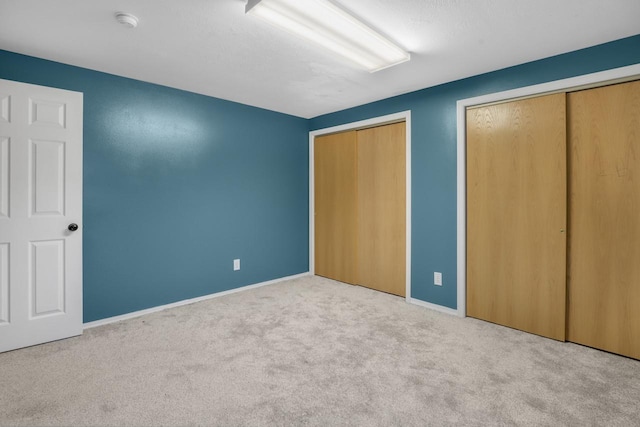 unfurnished bedroom featuring baseboards, multiple closets, and carpet floors