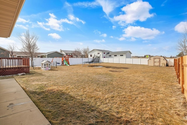 view of yard featuring a storage unit, an outbuilding, a trampoline, a fenced backyard, and a playground